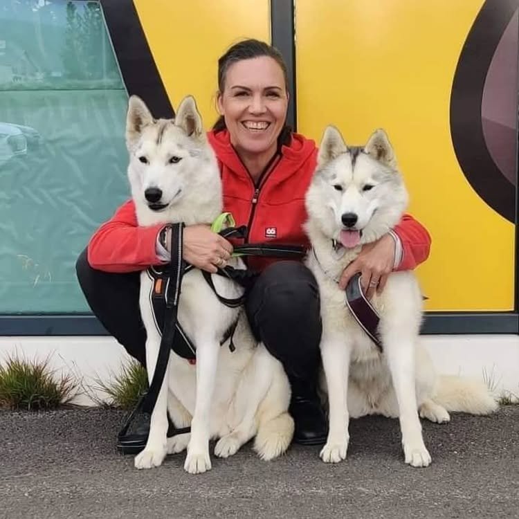 a woman smiling and sitting beside her two huskies